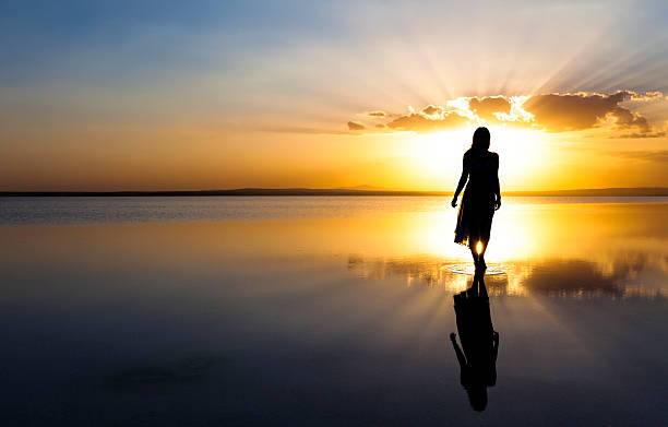ツインレイサイレント期間夕日の海辺を歩く女性