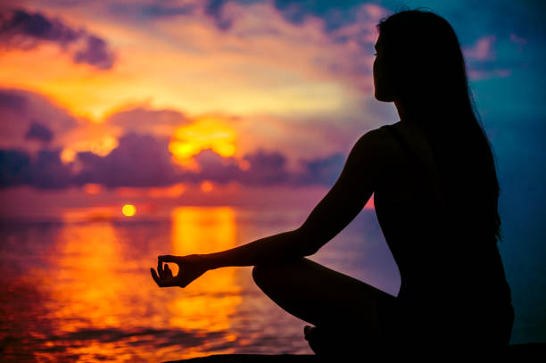 夕焼けの海辺で瞑想する女性