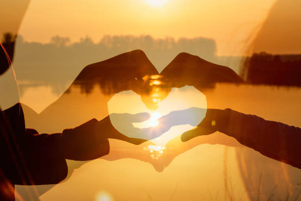 夕日の前で手でハートを作る男女