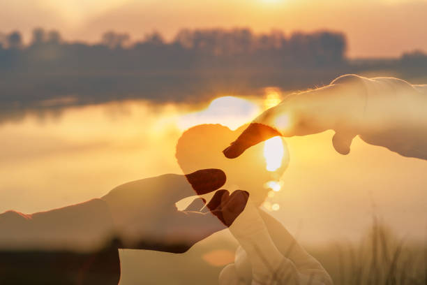 夕日とハートに指を合わせるカップル