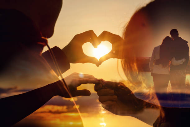 夕日をバックにお互いの手でハートを作るカップル
