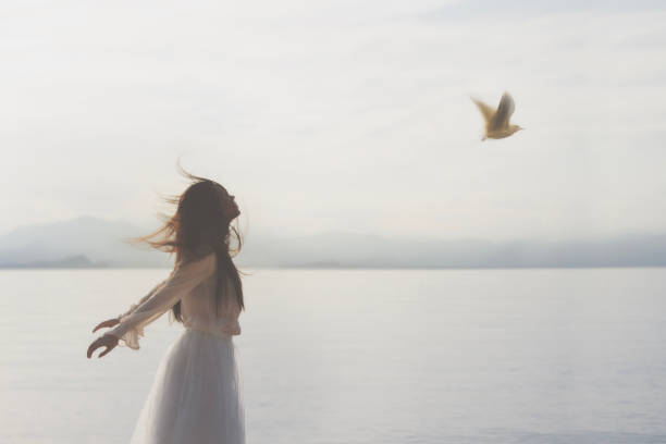 湖と両手を広げる女性に近づく鳩